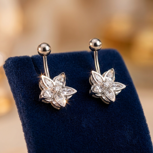 Pair of silver flower-shaped belly buttons on a blue stand with a blurred gold background